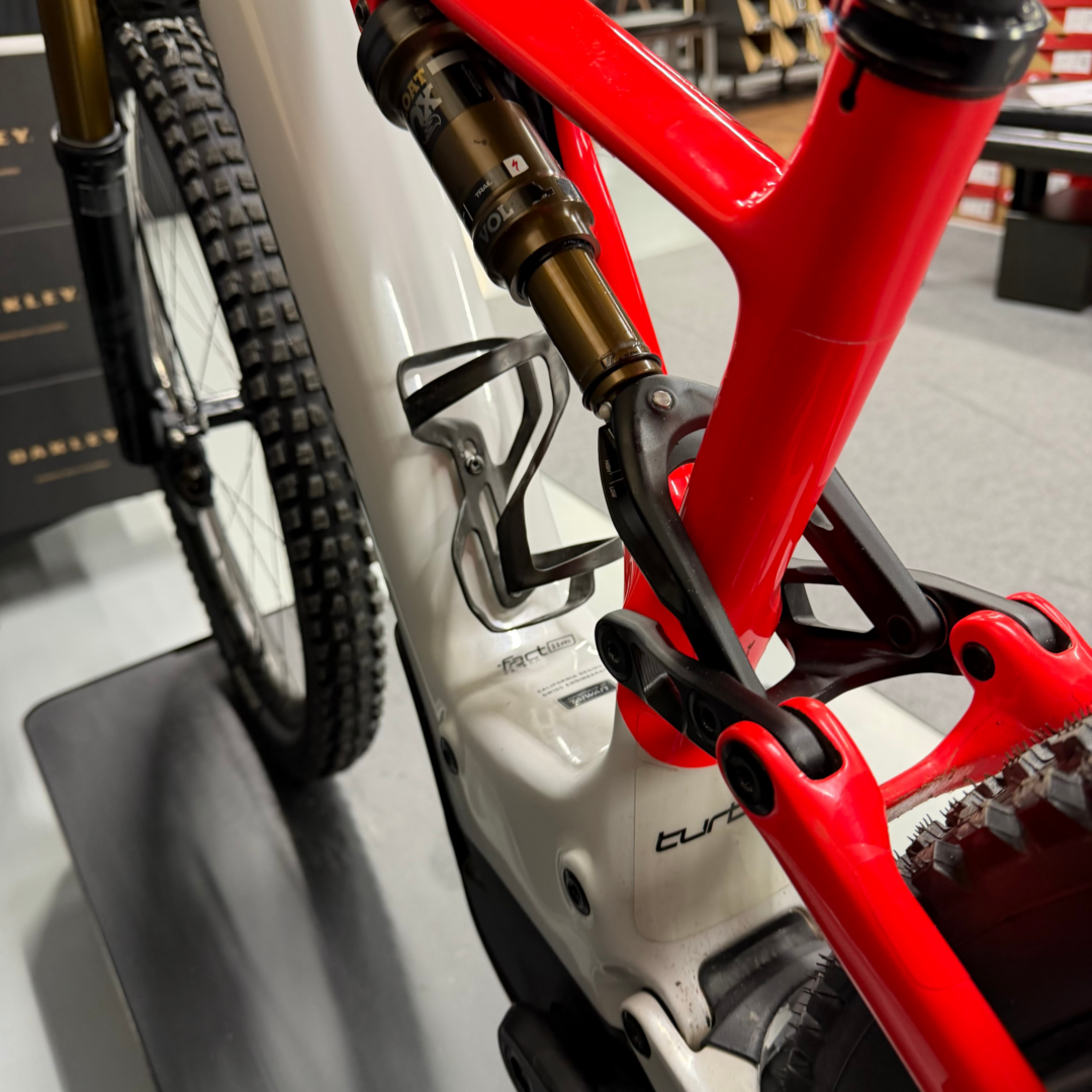 Close-up of a red mountain bike frame with a gold Fox rear suspension shock visible, mounted in a shop setting.