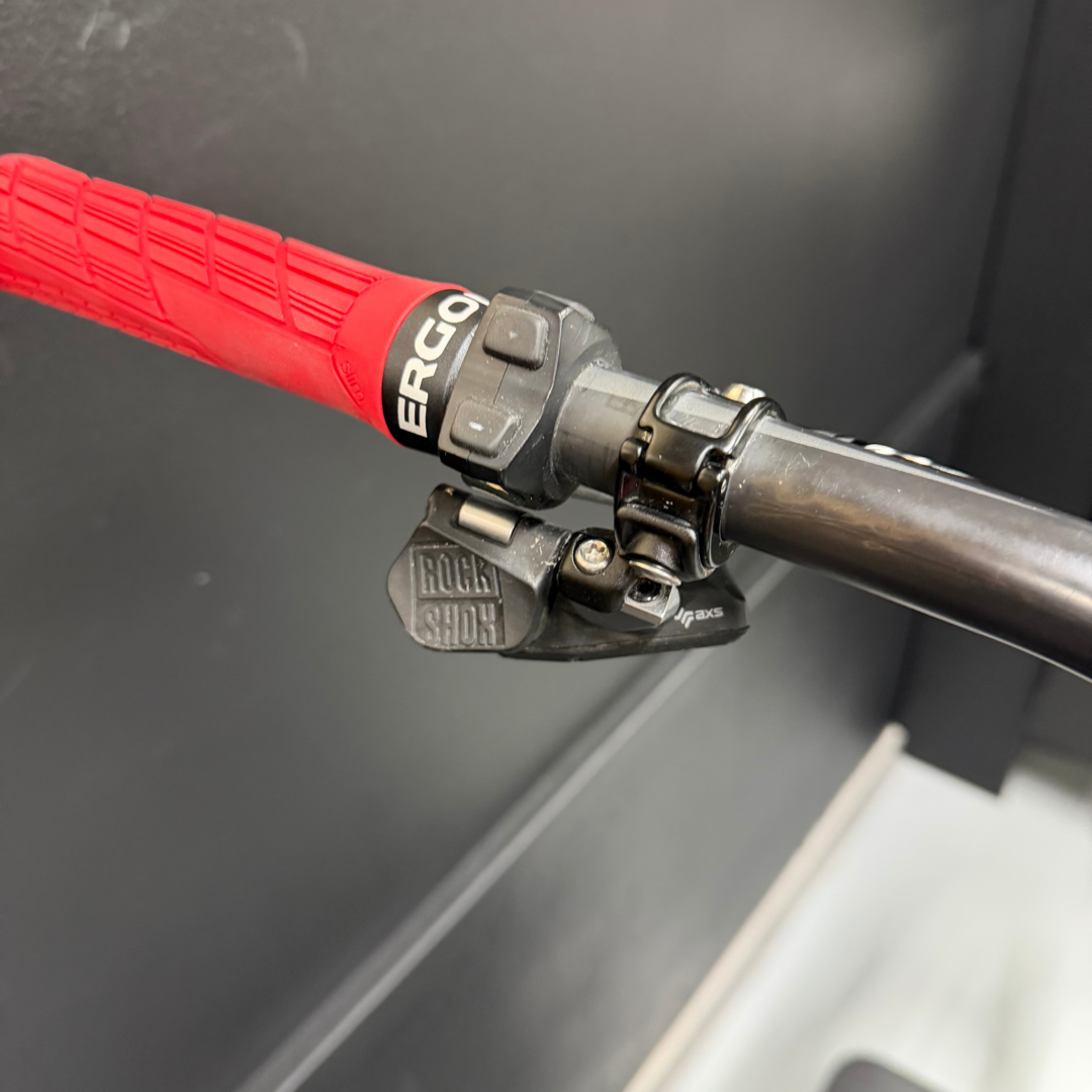 Close-up of a red bicycle handlebar grip with a gray brake/shift lever nearby on a dark frame.