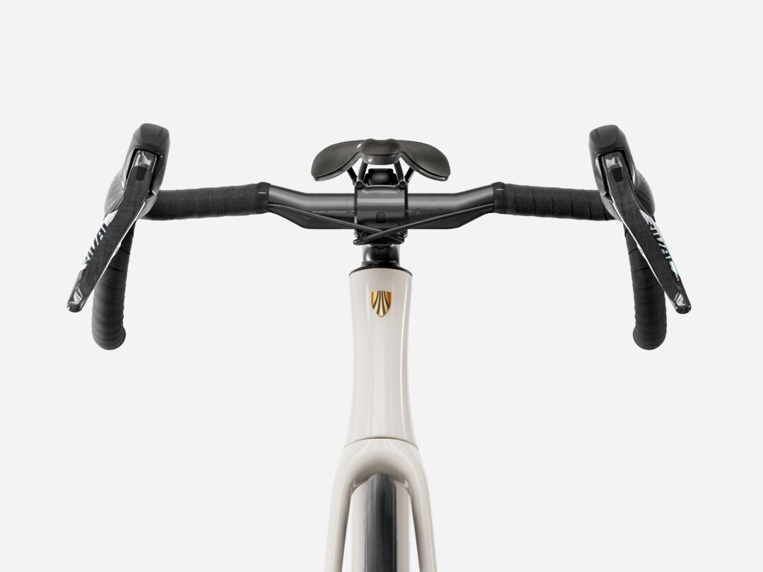 Top-down view of a road bike cockpit showing drop handlebars, black bar tape, integrated brake/shift levers, and a central stem with a shield logo