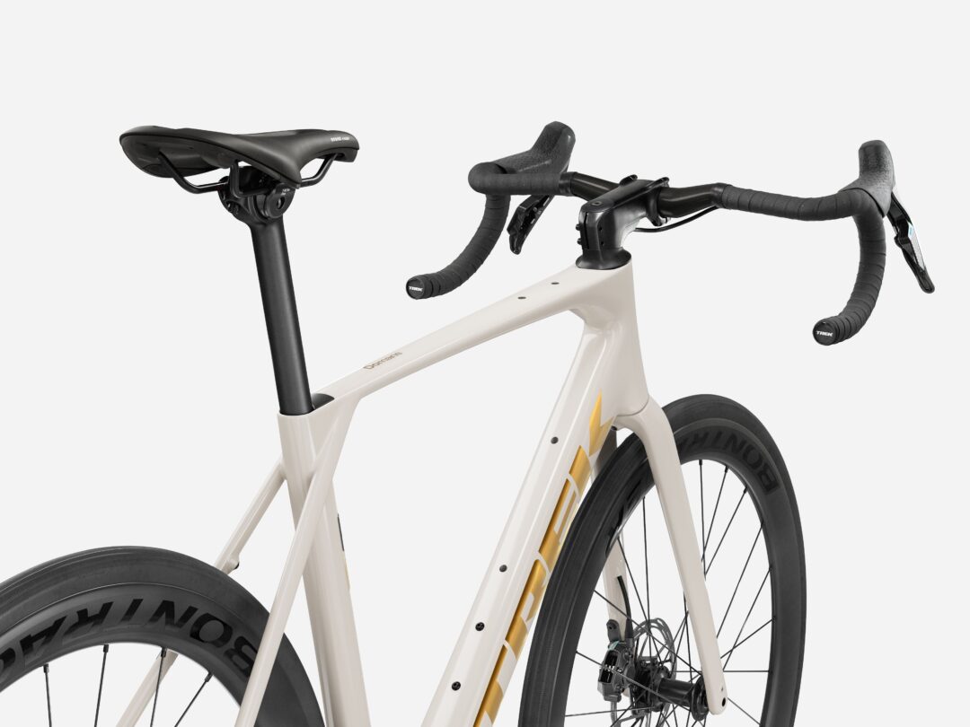 Close-up of a road bike cockpit: saddle, drop handlebars, and front frame seen from the side with a beige frame and black components.