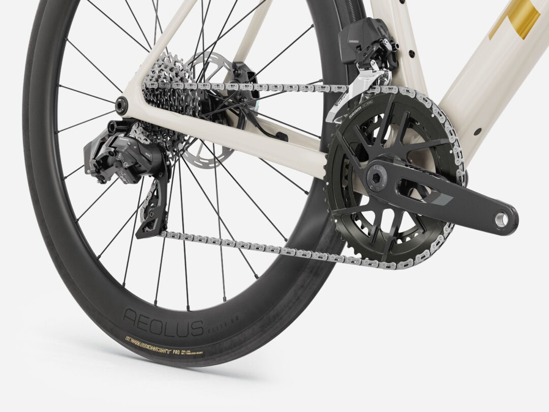 Close-up of a road bike drivetrain: rear derailleur, cassette, chain, crankset, and disc brake against a light frame.