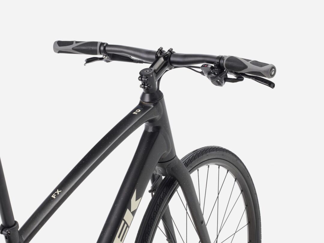 Black hybrid/road bike handlebar with ergonomic grips, brake levers, and dial, view of the front frame and wheel from a slight front angle