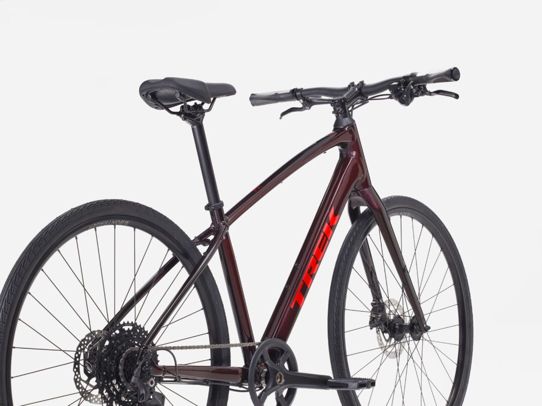 Side view of a maroon mountain bike showing the frame, handlebars, saddle, and front and rear wheels with a derailleur and disc brakes visible.
