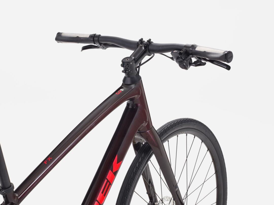 Close-up of a dark red mountain bike's handlebar, brake levers, and front wheel against a light background.