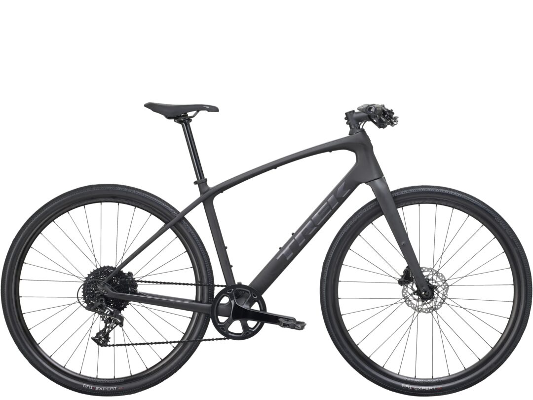 Partial view of a matte gray gravel bike showing the frame, crankset, rear derailleur, disc brakes, and two wheels visible from the middle to the front and rear.