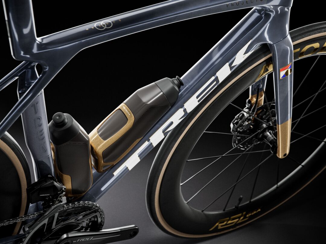 Close-up of a modern blue-gray electric road bike frame with an integrated battery and gold accents, against a dark background.