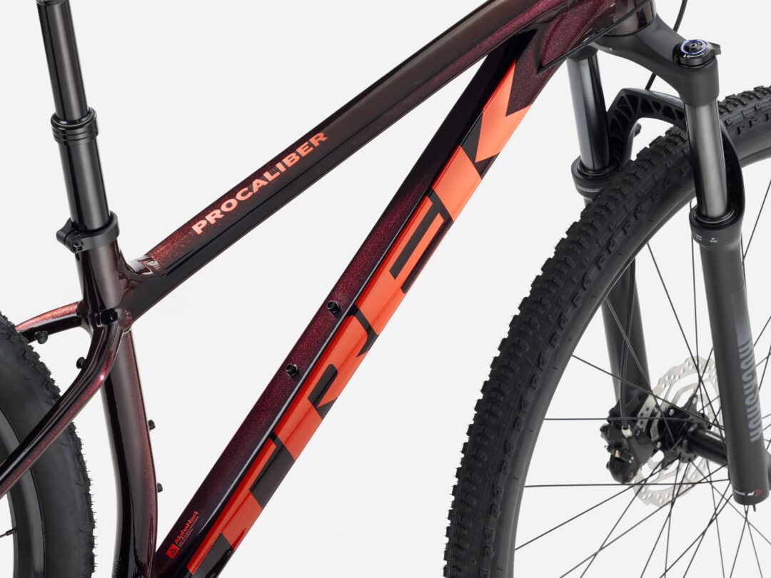 Close-up of a dark red/black Trek Procaliber mountain bike frame with orange graphics, showing the top tube and down tube meeting near the head tube.