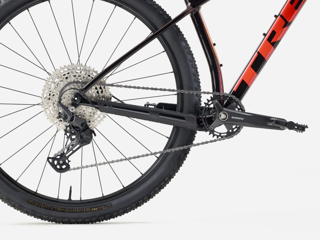 Close-up of a mountain bike's rear wheel showing cassette, chain, derailleur, and part of an orange frame edge.
